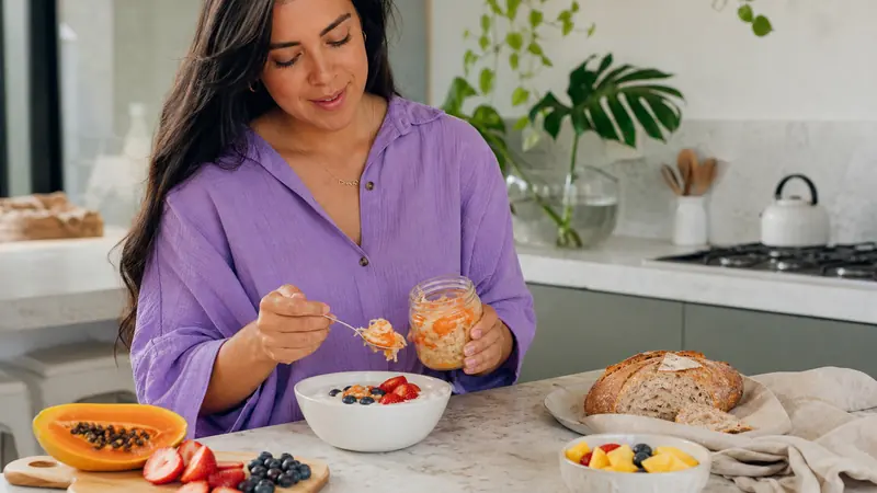 Mujer preparando yogur, frutas, vegetales fermentados y pan en una cocina luminosa
